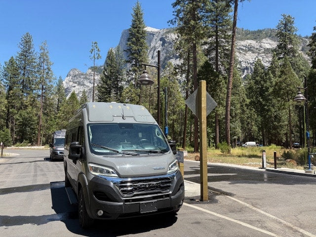 surrounded by tall trees and a massive rock face.|Two gray **RV rental** camper vans parked in a scenic national park — photo 5