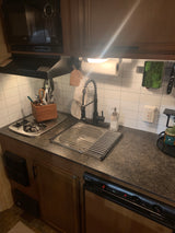 View of an RV rental kitchen: compact space with microwave, stovetop, sink, drying rack, and organized utensils.