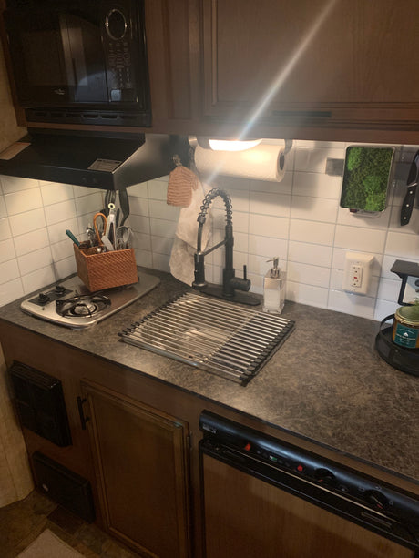 View of an RV rental kitchen: compact space with microwave, stovetop, sink, drying rack, and organized utensils.