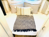 Cozy RV rental bed with neutral layered pillows, a patterned lumbar cushion, and a fringed dark throw blanket.