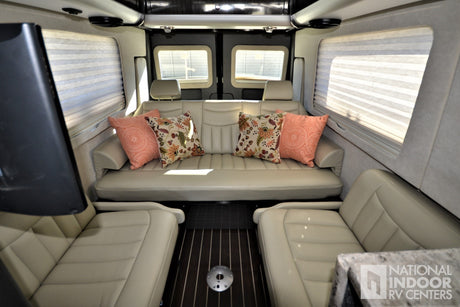 Plush RV rental interior: spacious lounge with cream sofa, decorative pillows, and facing seats on wood floor.