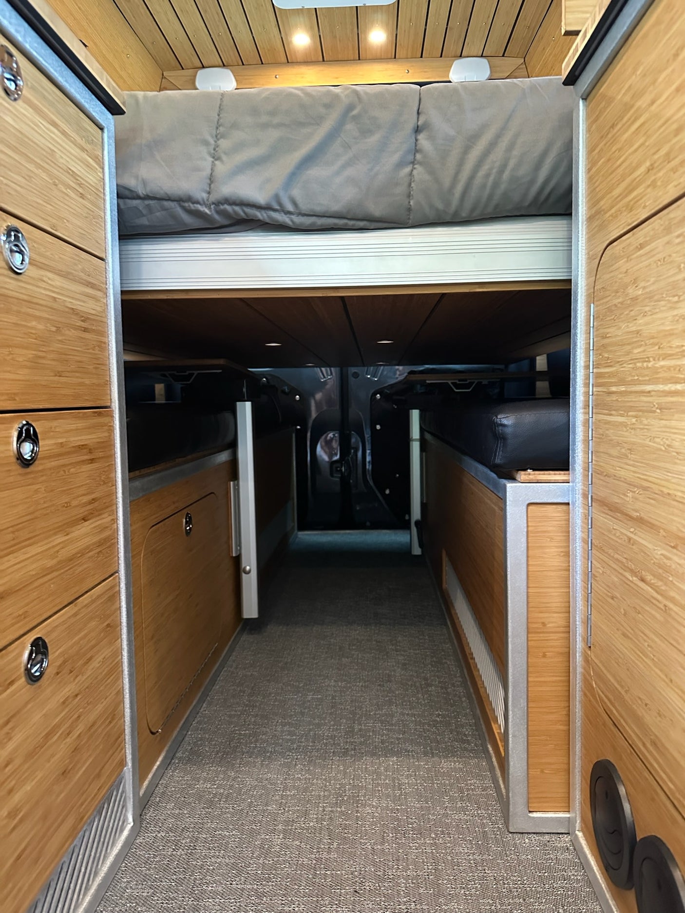 Inside an RV rental: Looking down a carpeted aisle between custom bamboo cabinetry to a raised bed & seating.