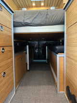 Inside an RV rental: Looking down a carpeted aisle between custom bamboo cabinetry to a raised bed & seating.