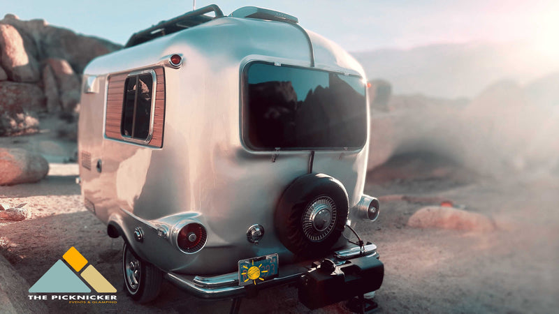Vintage RV rental for glamping & events! This silver travel trailer shines in a rocky desert landscape at sunset. — photo 9