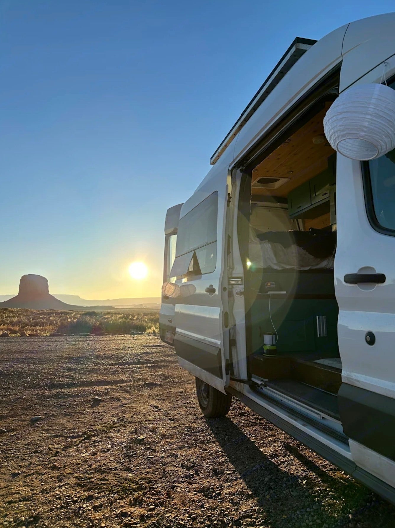 This RV rental offers sunset views over a desert mesa. Its open side door reveals a cozy, wood-paneled interior.