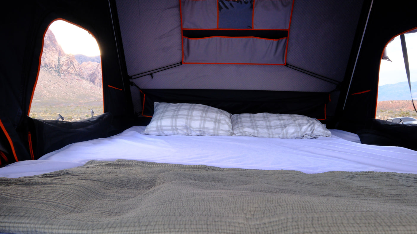 Inside an rv rental rooftop tent: a comfy bed awaits with a stunning mountain landscape outside.