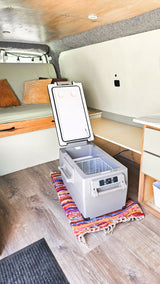 Cozy RV rental interior with a portable cooler, comfy bench, and wood flooring. Perfect for your next adventure!