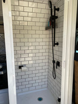 Clean, modern RV rental shower with white subway tiles, matte black fixtures, and a toilet paper holder. Compact interior design.