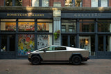 A striking Tesla Cybertruck, resembling a unique RV rental, sits on a brick street outside an art gallery. Electric adventure awaits.