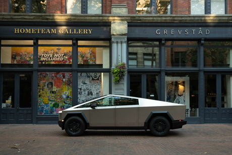 A striking Tesla Cybertruck, resembling a unique RV rental, sits on a brick street outside an art gallery. Electric adventure awaits.