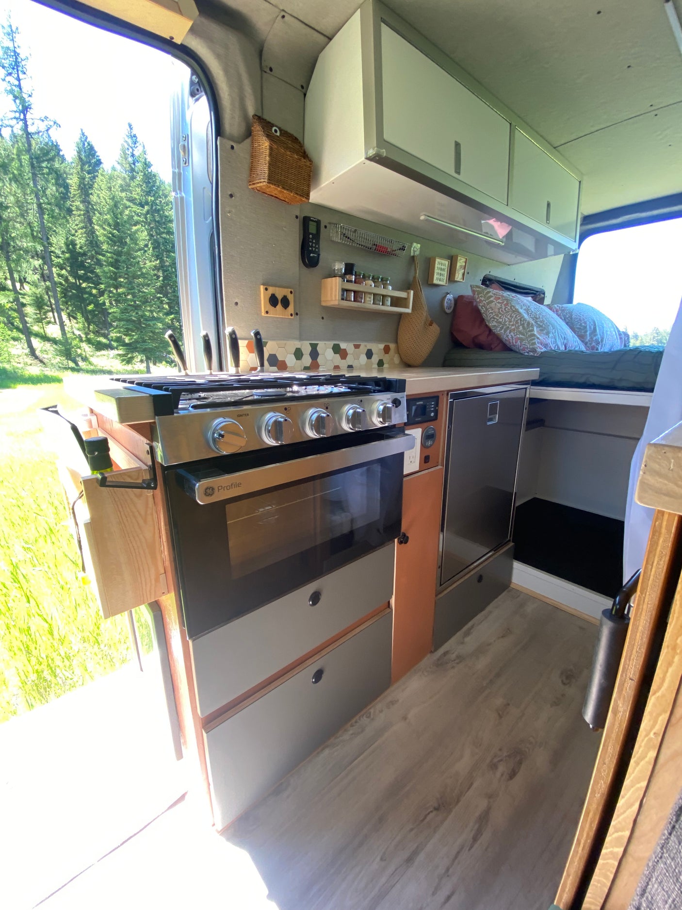 Explore this RV rental's clever camper van interior, featuring a full kitchen with oven, fridge, and a comfy bed, overlooking nature.
