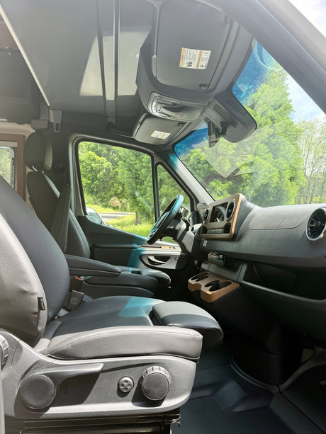 Explore the spacious driver's cabin of this RV rental, featuring comfortable gray seats, a modern dashboard, and scenic views.
