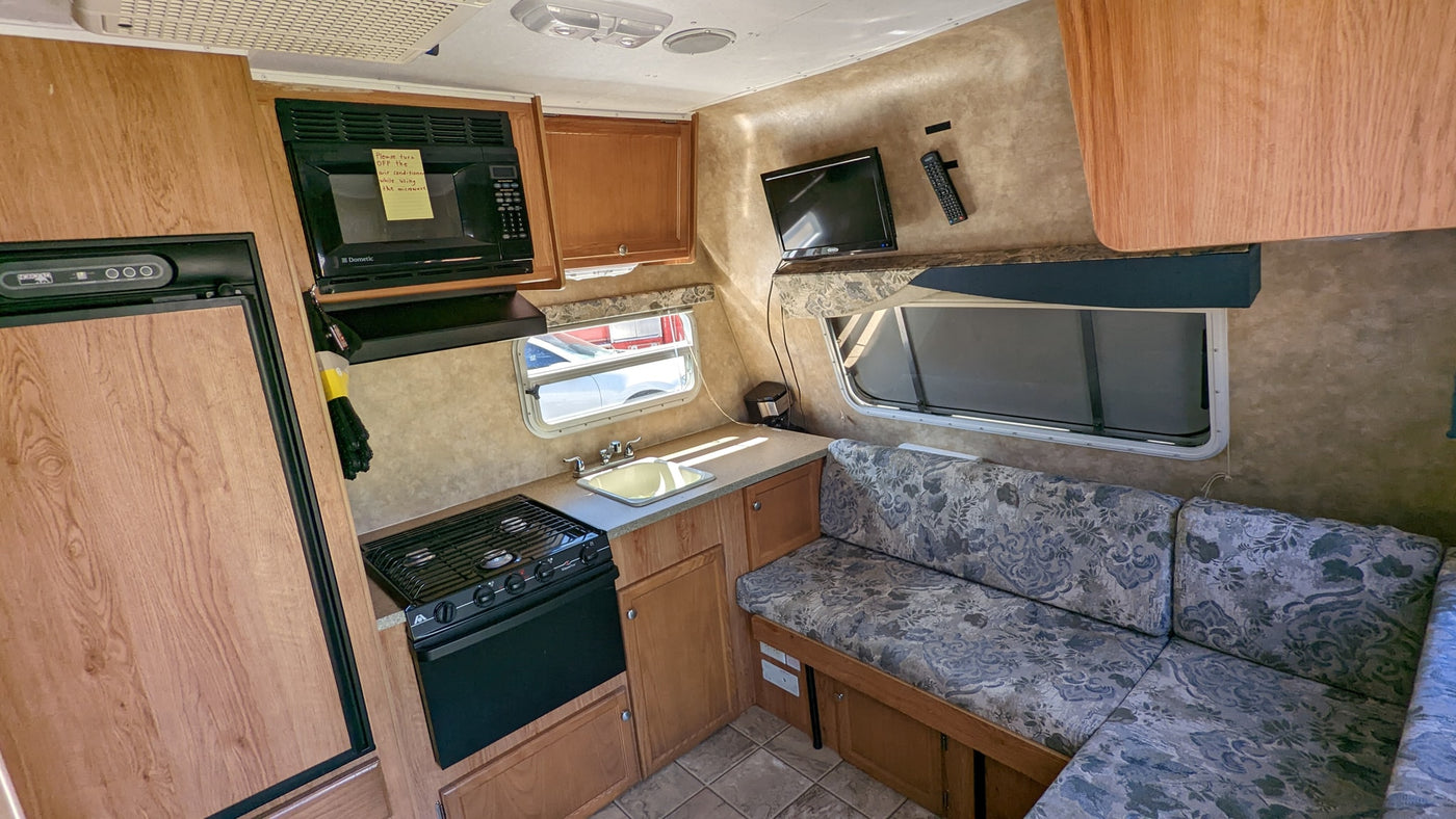 This rv rental interior features a compact kitchenette with microwave, stove, sink, fridge, and a cozy dinette. Ready for your trip! — photo 17