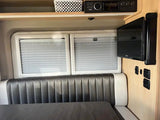 Inside an RV rental: a comfortable gray dinette with white trim, pleated blinds, TV, and entertainment system.