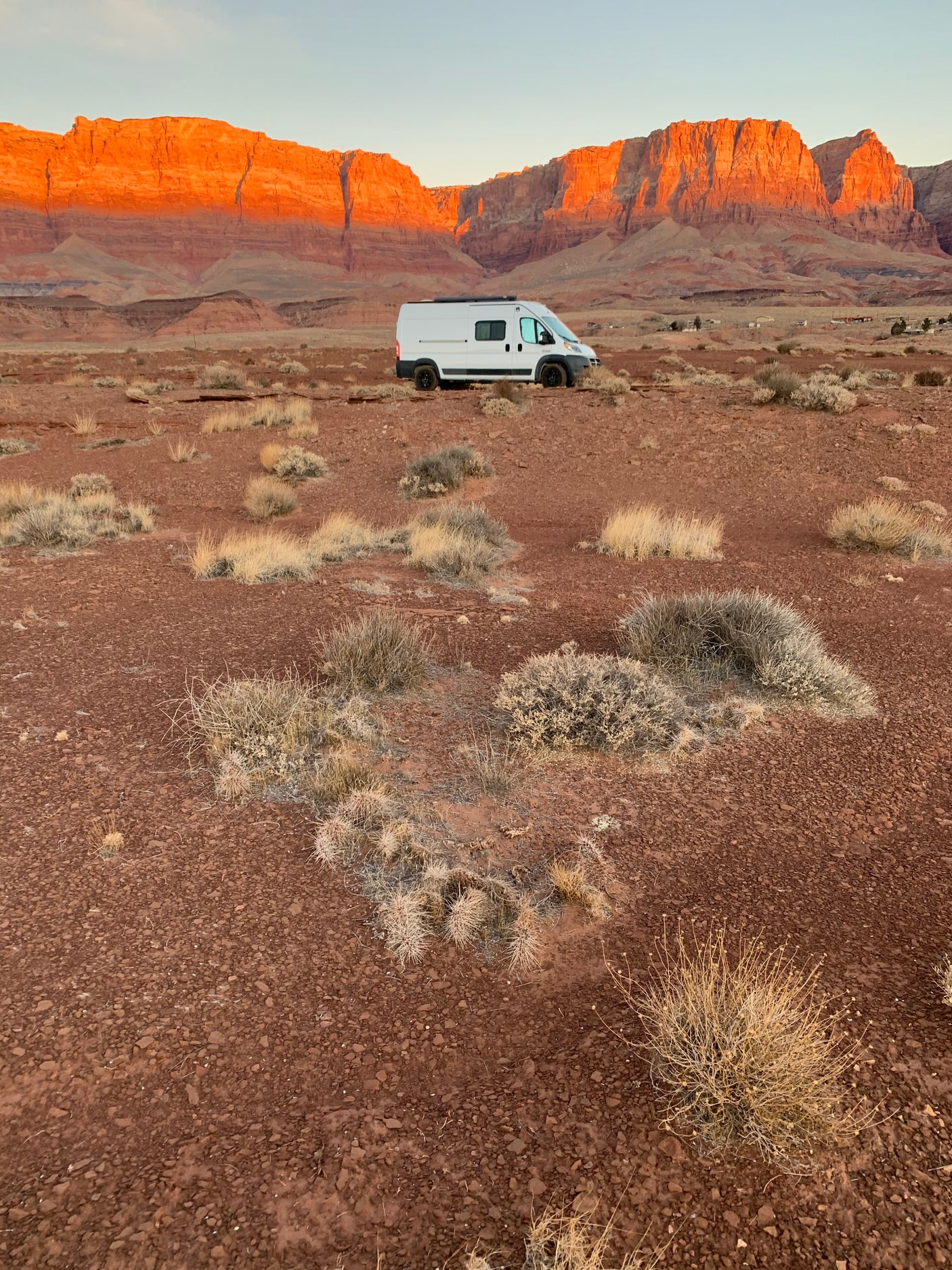 RV rental adventure: White van in a vast red desert, with majestic red rock cliffs glowing under golden hour light.
