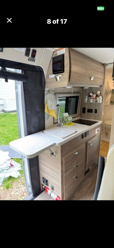 Functional kitchen in this RV rental, with sink, microwave, cabinets, and pull-out counter. Fire extinguisher visible for safety.