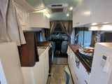 Stylish RV rental interior with a well-equipped kitchen, white cabinetry, and light blue ceiling. Ready for adventure.