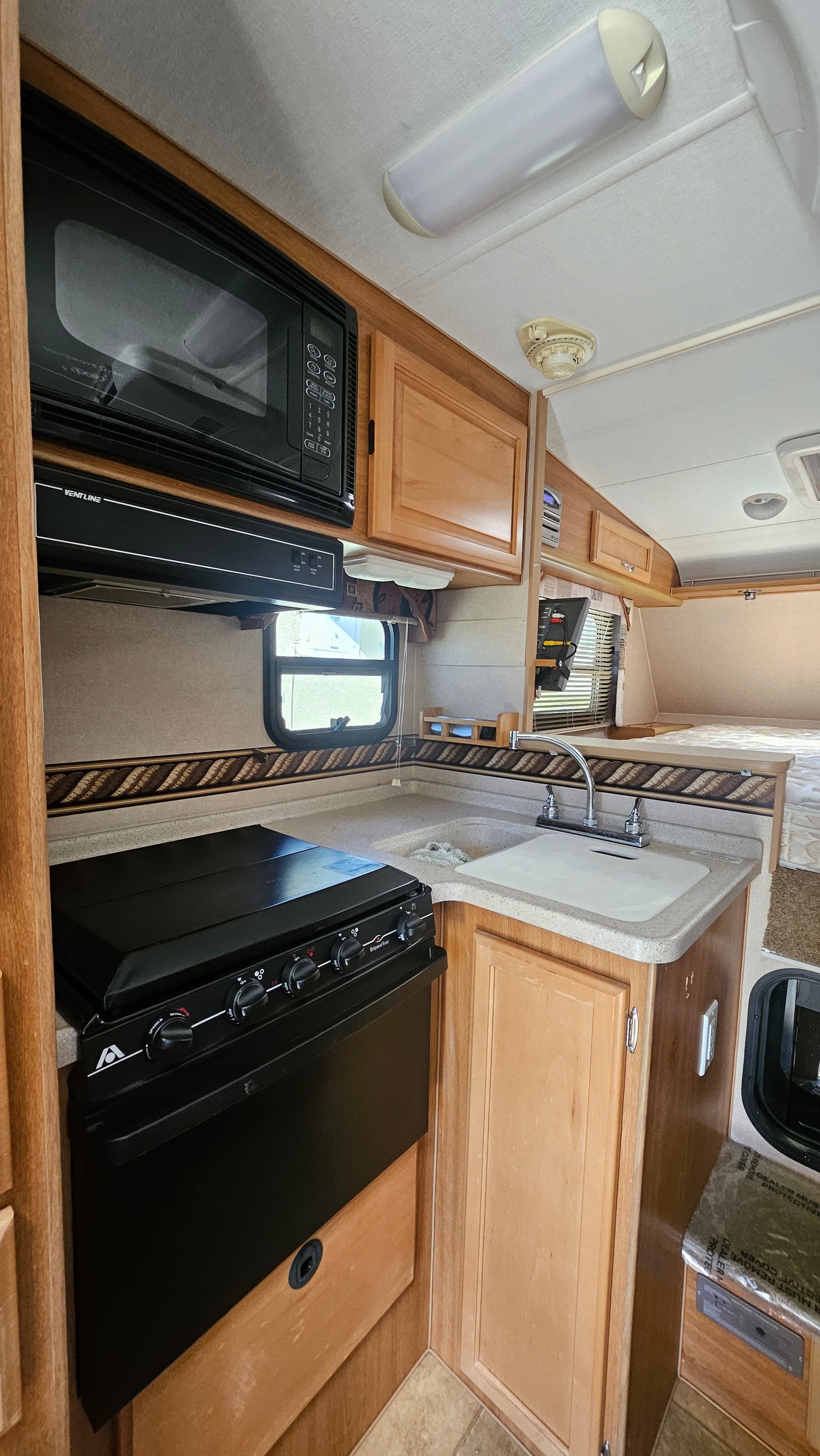 Clean RV rental kitchen with microwave, stove, sink, and wooden cabinets. Rear sleeping area visible.