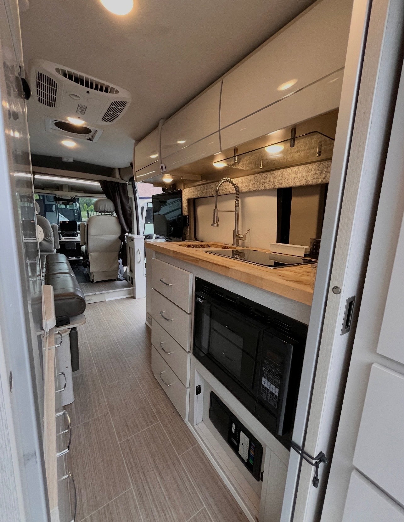 Explore this modern RV rental's galley kitchen, featuring a built-in sink, induction cooktop, microwave, and elegant storage.