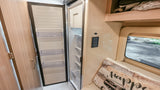 This RV rental interior features an open, compact refrigerator, a control panel, and a "Happy Camper" pillow on a bench seat.