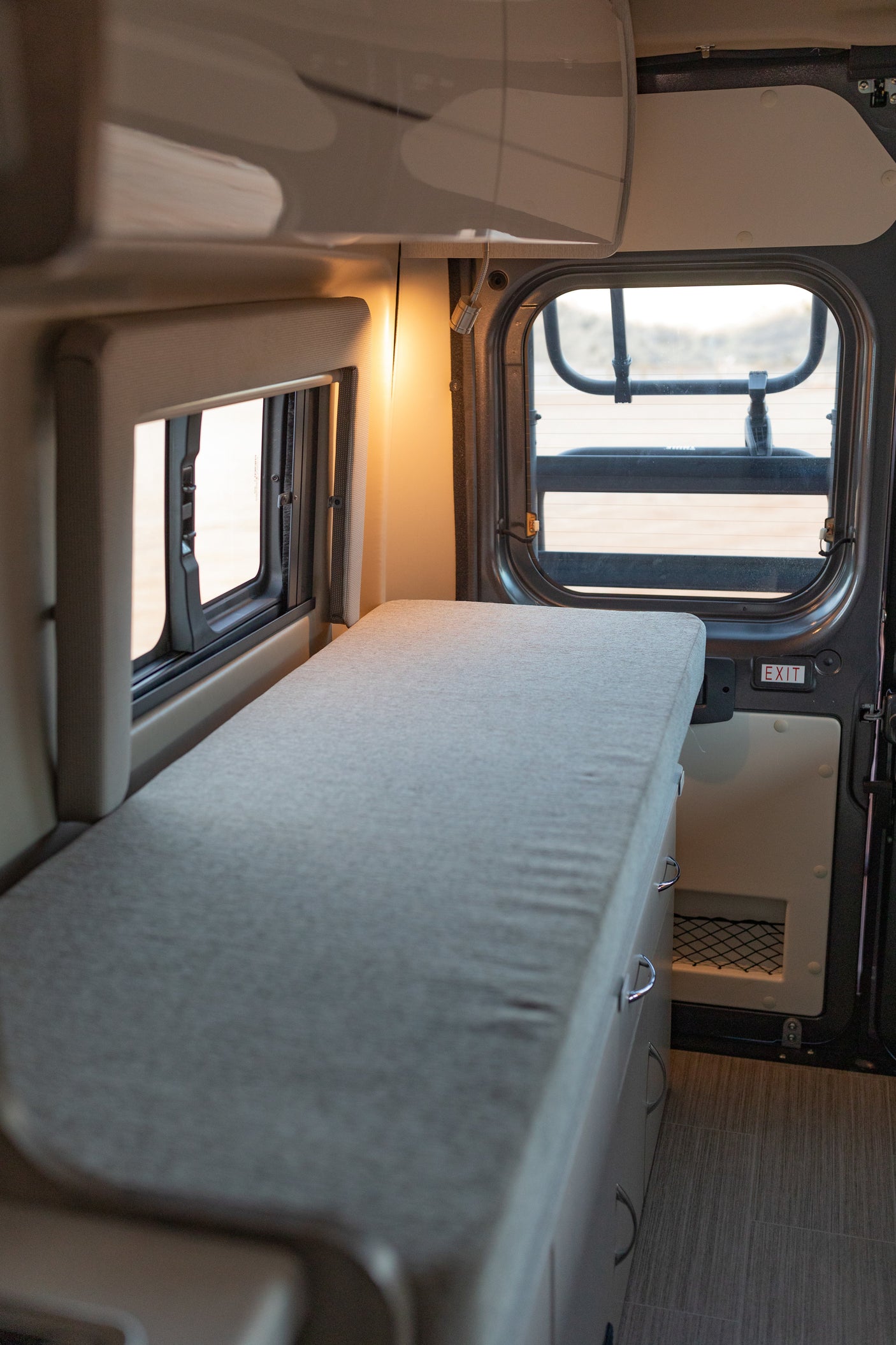 An inviting RV rental interior featuring a long bed/lounge, overhead storage, and large windows for scenic views.