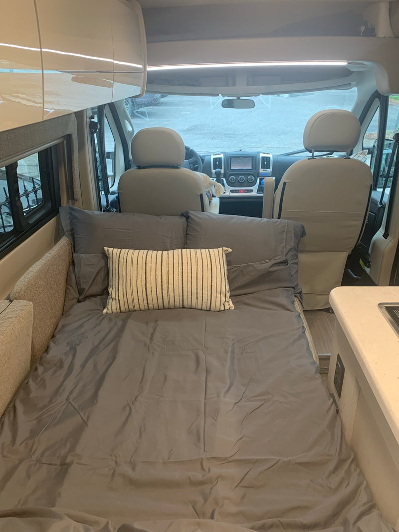 Cozy RV rental interior: Full-size bed with grey bedding, compact kitchen, and front cockpit of a camper van. — photo 16