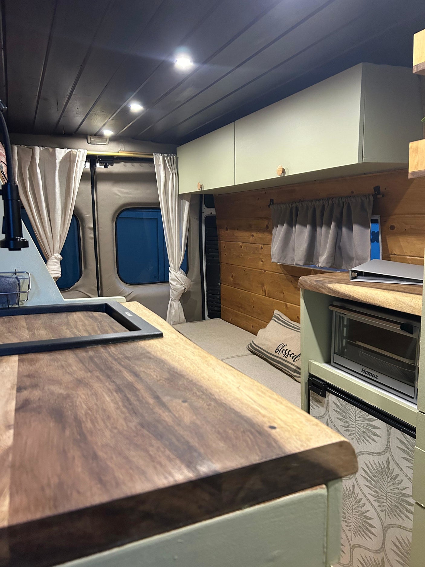 RV rental interior featuring a kitchenette with wood counters, sink, oven, fridge, and a cozy bed area.