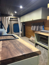 RV rental interior featuring a kitchenette with wood counters, sink, oven, fridge, and a cozy bed area.