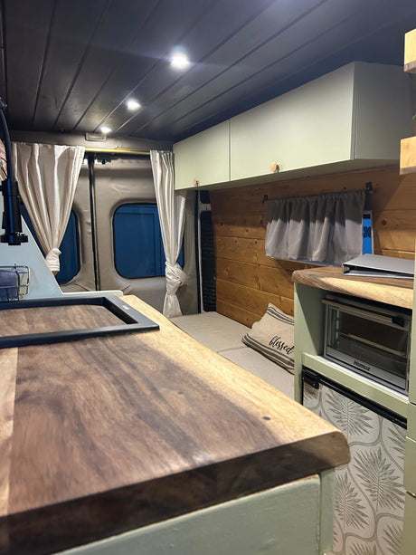 RV rental interior featuring a kitchenette with wood counters, sink, oven, fridge, and a cozy bed area.