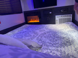 Experience comfort in this RV rental bedroom with a cozy bed, electric fireplace, TV, and AC unit.