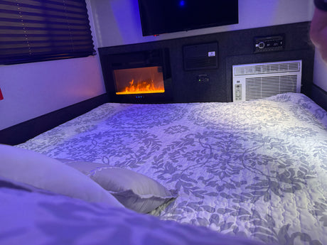 Experience comfort in this RV rental bedroom with a cozy bed, electric fireplace, TV, and AC unit.