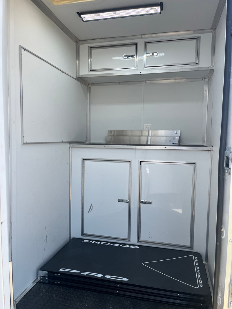 Compact RV rental interior: overhead LED, white cabinets, counter, and a folded GoPong Pro table on the floor. — photo 7