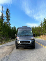 Explore nature with this RV rental camper van on a scenic forest road. Two people enjoy the journey.