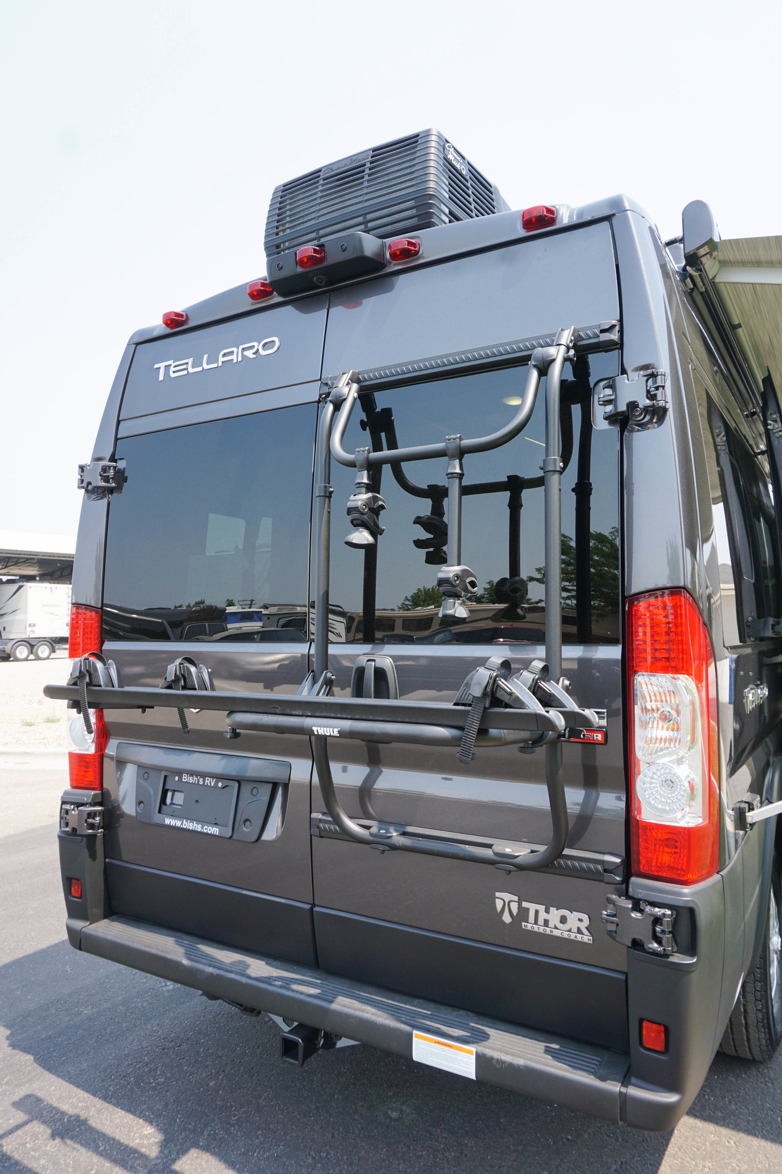 Rear view of a dark gray Thor Tellaro RV rental, equipped with a Thule bike rack, roof AC unit, and tow hitch.