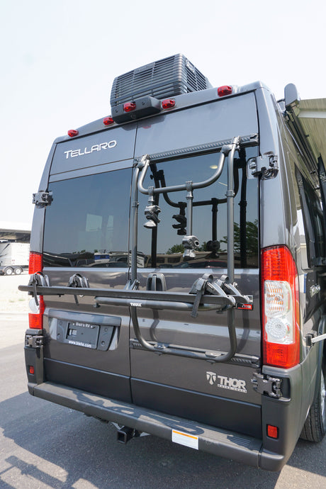Rear view of a dark gray Thor Tellaro RV rental, equipped with a Thule bike rack, roof AC unit, and tow hitch.
