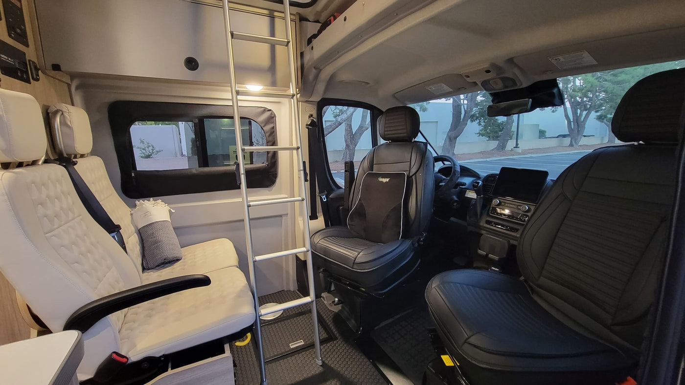 Modern RV rental interior with black swivel front seats, light rear lounge seats, and a bunk access ladder. — photo 2