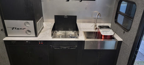 Inside an RV rental: a compact kitchen with a two-burner stovetop, sink, ice maker, and refrigerator.