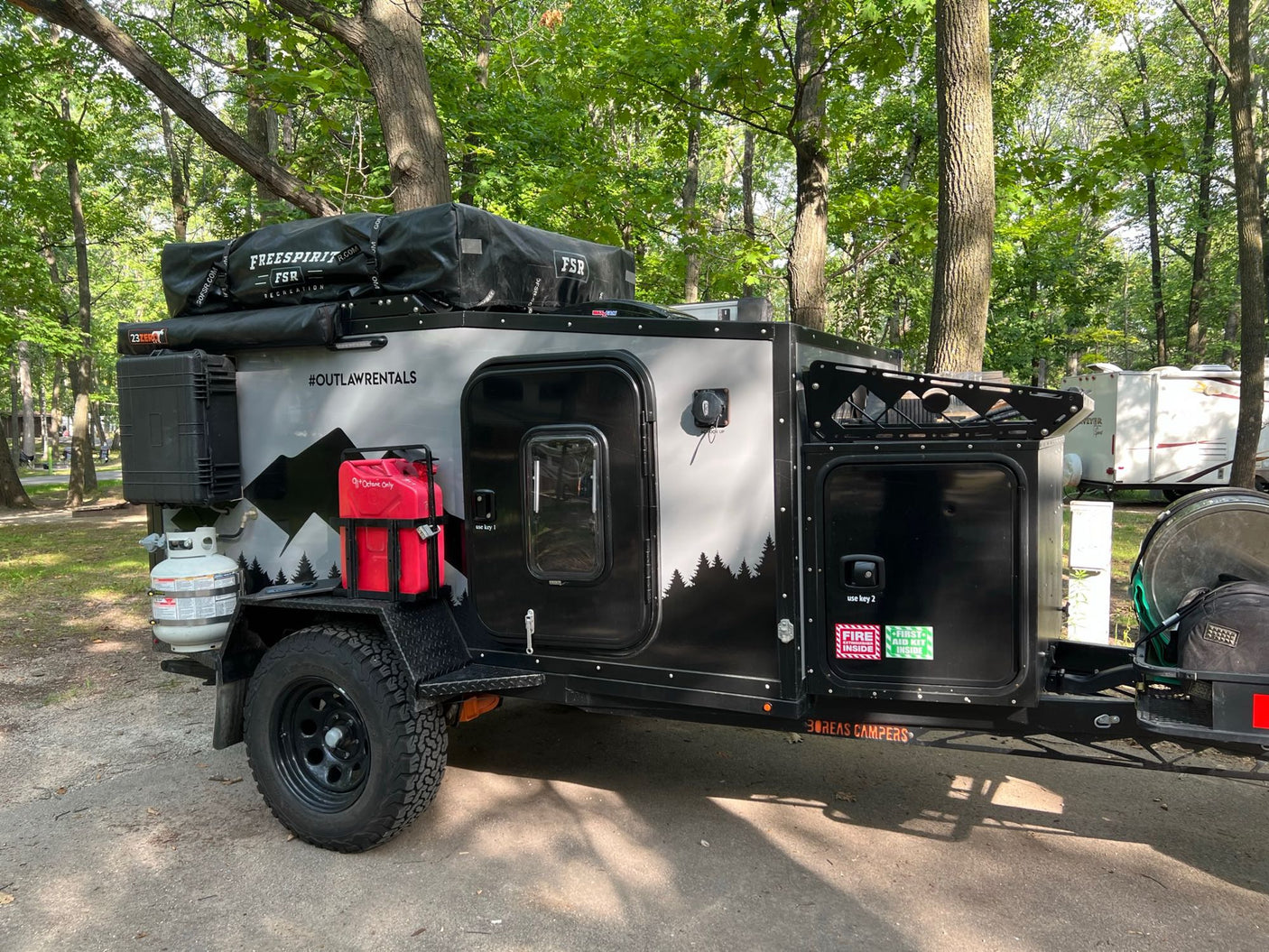 Explore nature with this rugged off-road camper trailer, an ideal rv rental. Parked in woods, it features a rooftop tent.