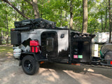 Explore nature with this rugged off-road camper trailer, an ideal rv rental. Parked in woods, it features a rooftop tent.