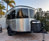 Sleek Airstream travel trailer for RV rental, parked on a brick patio amidst palm trees at sunset.
