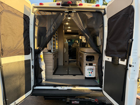 RV rental: Rear view of open camper van doors with a mesh screen, showing interior and a water management panel.