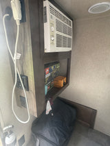 Cozy RV rental interior with a wall AC unit, control panel, and storage for camping gear, including an air pump.