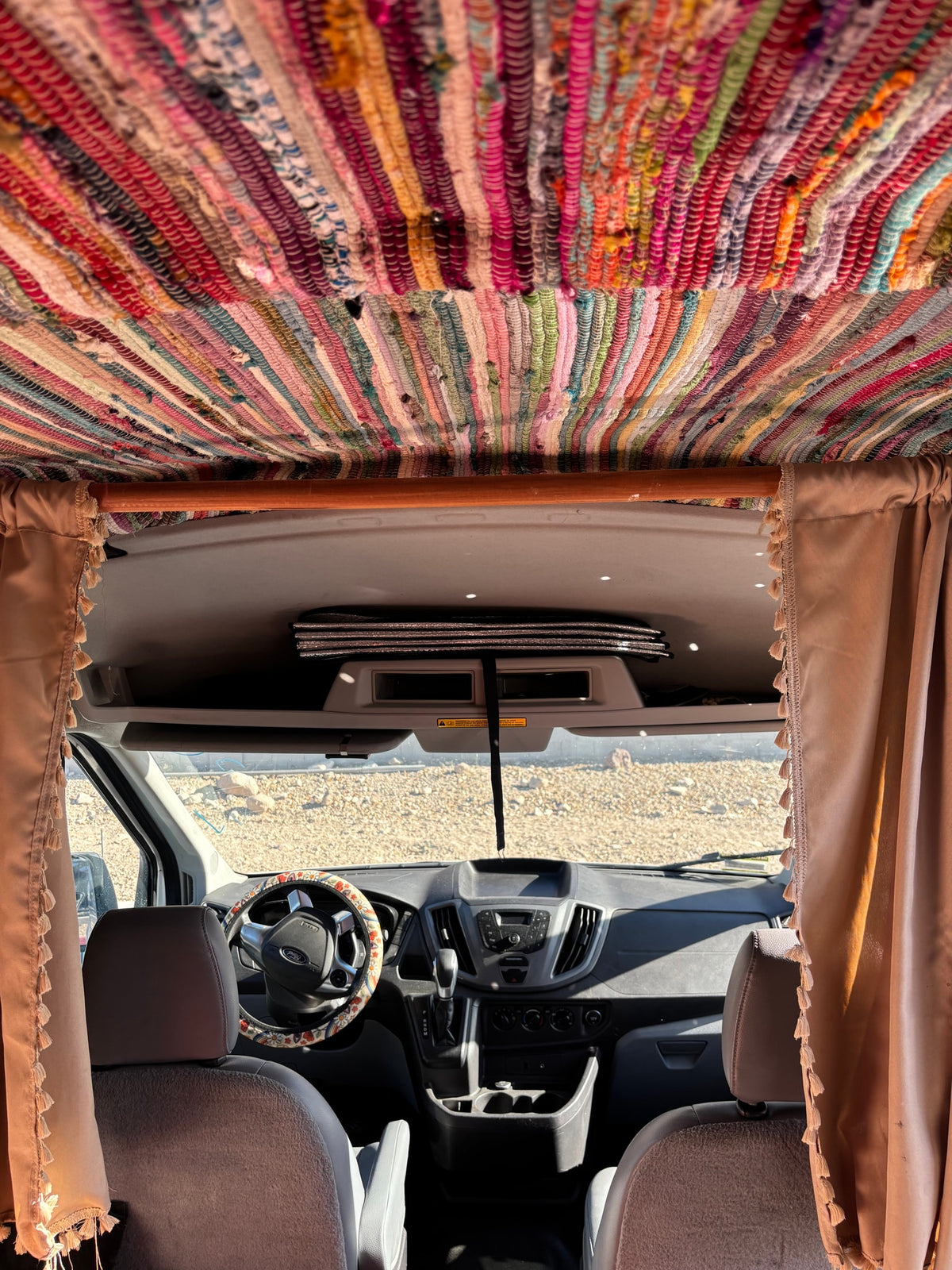 Cozy RV rental interior, showing a colorful rag rug ceiling & front cabin with dashboard & outdoor view. — photo 2