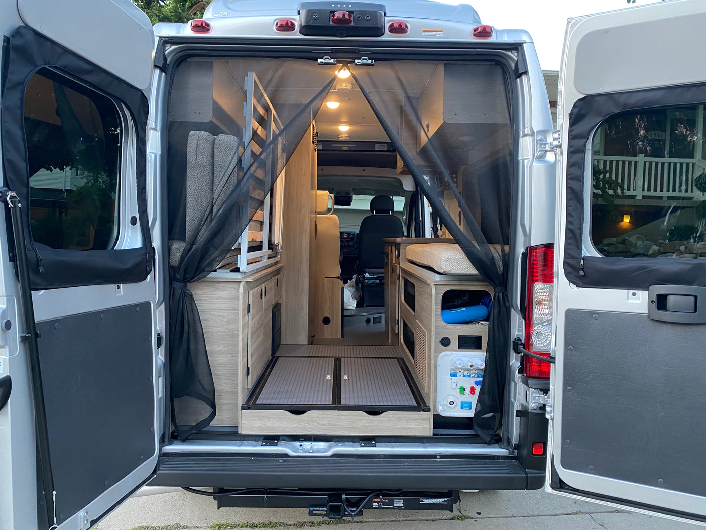 This rv rental reveals a camper van's spacious rear interior through open doors, featuring a mesh screen, compact living, and utilities.