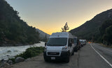 RV rental vans parked by a scenic river in the mountains at sunset. An outdoor adventure road trip caravan.