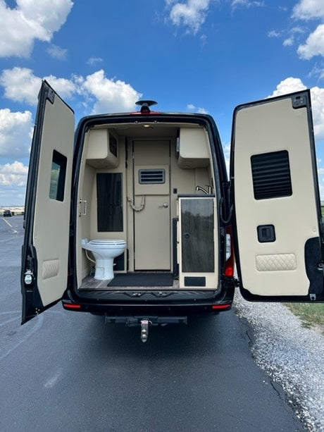 Explore with an RV rental! Rear of a camper van with open doors revealing a toilet, sink, and interior living space.