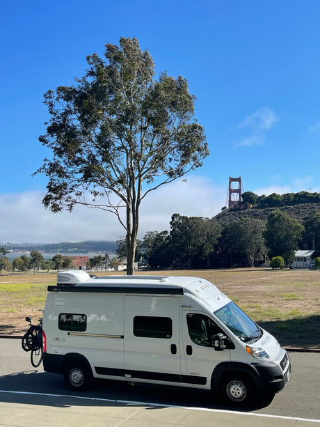 This white Solis camper van, an ideal rv rental, is parked overlooking a field and the foggy Golden Gate Bridge in San Francisco.
