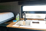 Cozy RV rental interior with a bed, a compact kitchen featuring a Kraus sink, Mrs. Meyer's soaps, and a window.