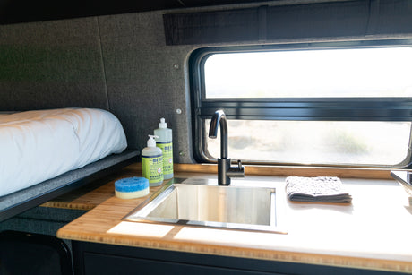 Cozy RV rental interior with a bed, a compact kitchen featuring a Kraus sink, Mrs. Meyer's soaps, and a window.