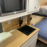 RV rental kitchen: compact microwave, black sink, wood counter, and bunk beds in the background.